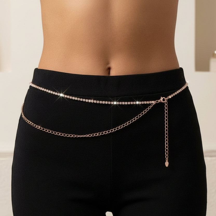 A close-up of a model's lower torso wearing a delicate rose gold chain waist belt over black leggings, with a softly blurred indoor background.